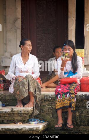 Templegoers balinais en robe de fête pour les célébrations de la fête de Galungan, temple de Sakenan, Bali, Indonésie. Jeune femme avec un oiseau en cage. Banque D'Images