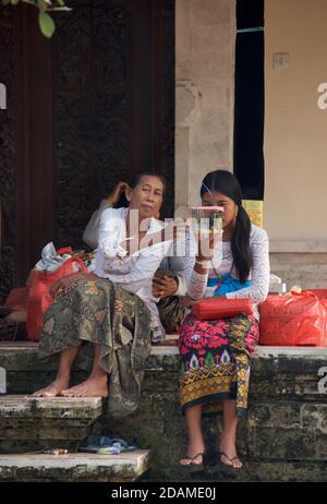 Templegoers balinais en robe de fête pour les célébrations de la fête de Galungan, temple de Sakenan, Bali, Indonésie. Jeune femme avec un oiseau en cage. Banque D'Images