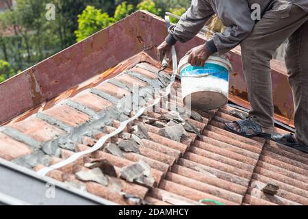 Un ouvrier asiatique sécurise les tuiles de toit avec du ciment sur le vieux bâtiment Banque D'Images