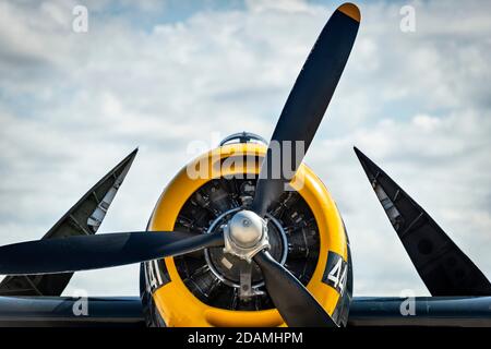 Un avion porte-avions bleu marine de la Seconde Guerre mondiale, avec un capot jaune, avec des ailes repliées contre un ciel bleu et nuageux Banque D'Images