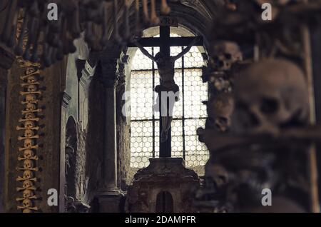 Kutna Hora, République tchèque, 14 mai 2019 : la crucifixion de Jésus-Christ à la fenêtre et en gros plan brouille humaine floue avec os dans la bouche au premier plan. Décoration par crâne humain et os. Église de Kostnice Banque D'Images