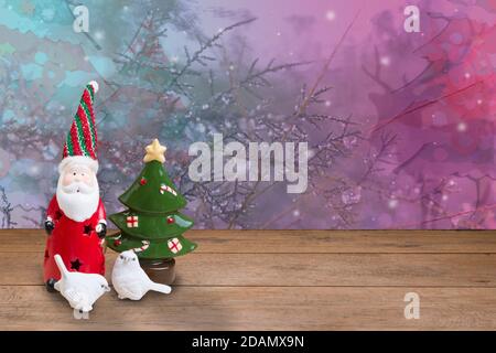 Le père noël en céramique et deux petits oiseaux blancs sur un parquet avec un arbre à baptêmes en hiver sur fond. Banque D'Images