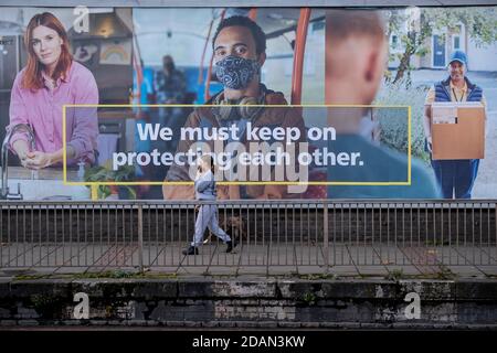 Un londonien du sud passe devant une annonce du NHS (National Health Service) demandant au public de se protéger les uns les autres avec des revêtements faciaux sur Queenstown Road à Battersea, lors du deuxième confinement de la pandémie du coronavirus au Royaume-Uni, lorsque tous les détaillants et entreprises, à l'exception des principaux, restent fermés conformément aux règles de restriction du gouvernement, Le 13 novembre 2020, à Londres, en Angleterre. Banque D'Images