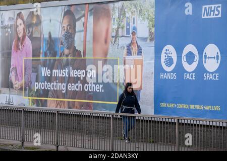 Un londonien du sud passe devant une annonce du NHS (National Health Service) demandant au public de se protéger les uns les autres avec des revêtements faciaux sur Queenstown Road à Battersea, lors du deuxième confinement de la pandémie du coronavirus au Royaume-Uni, lorsque tous les détaillants et entreprises, à l'exception des principaux, restent fermés conformément aux règles de restriction du gouvernement, Le 13 novembre 2020, à Londres, en Angleterre. Banque D'Images