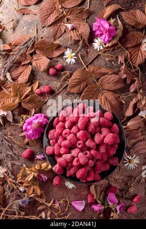 Framboises fraîches juteuses sur une assiette noire. L'été encore la vie avec, framboises, fleurs et herbes de prairie. Vue du dessus. Banque D'Images