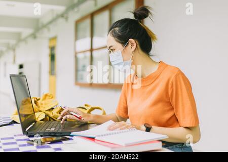 Femme asiatique adolescente travaillant seule portant un masque facial à l'université. Banque D'Images