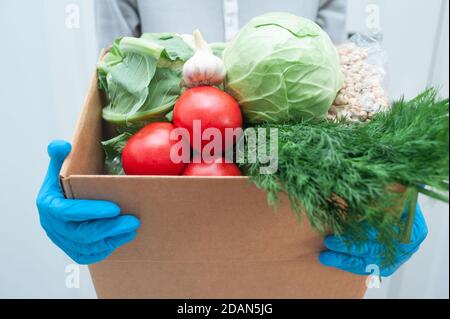 Le volontaire en gants tient la boîte de don de nourriture légumes pour aider les malades ou les pauvres. Donner la boîte avec les denrées alimentaires Banque D'Images