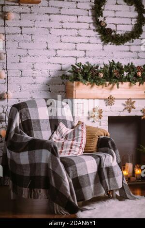 Fauteuil recouvert d'une couverture confortable, debout près de la cheminée décorée d'une guirlande de Noël. Banque D'Images