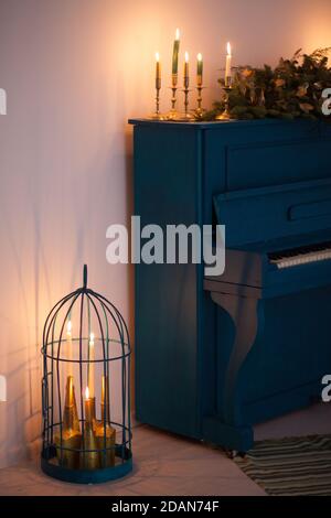 Un vieux piano de couleur bleue, décoré d'une longue guirlande de Noël de branches de sapin et de bougies allumées pour célébrer les vacances. Éléments dorés de f Banque D'Images