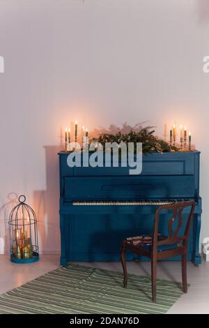 Un vieux piano de couleur bleue, décoré d'une longue guirlande de Noël de branches de sapin et de bougies allumées pour célébrer les vacances. Éléments dorés de f Banque D'Images