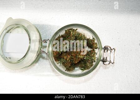 bourgeons secs de marijuana dans un pot en verre ouvert un arrière-plan clair Banque D'Images