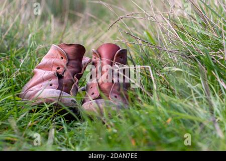 Une paire de bottes en cuir d'époque faites à la main pour enfant dans une herbe verte longue photographiée dans le Kent, au Royaume-Uni. Banque D'Images