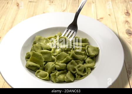 ravioli del plin vert, pâtes de l'italie de langhe, faites avec des pâtes aux œufs et des légumes aux épinards avec une fourchette élevant un ravioli sur le backgroun rustique en bois Banque D'Images