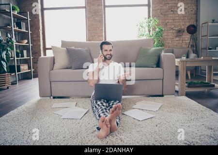 Photo de l'homme positif responsable marketing assis tapis de sol travail appel à distance sur un ordinateur portable smartphone un collègue dit parler dire parler nouvelles de démarrage covid-19 Banque D'Images