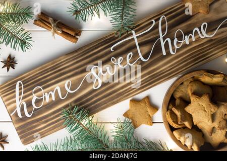 Maison Sweet Home lettrage panneau en bois brûlé avec biscuit au pain d'épice, branches d'arbre de Noël, bâtons de cannelle et anis sur la surface blanche. Pose à plat Banque D'Images