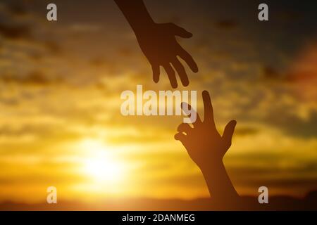 Silhouette de donner une main d'aide, d'espoir et de soutien l'un l'autre sur fond de coucher de soleil. Concept d'aider les mains et de développer une amitié. Banque D'Images