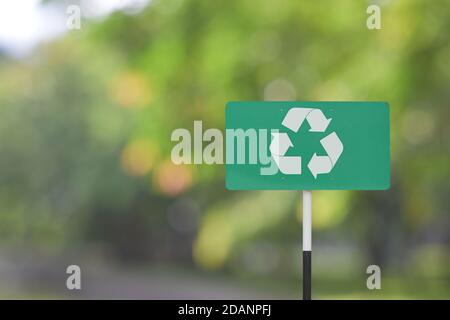 Un panneau de signalisation avec logo de recyclage sur fond vert flou. Banque D'Images