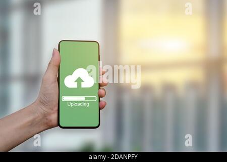 Gros plan de la main tenant un smartphone mobile avec chargement sur le Cloud pour stocker des données sur le serveur. Banque D'Images