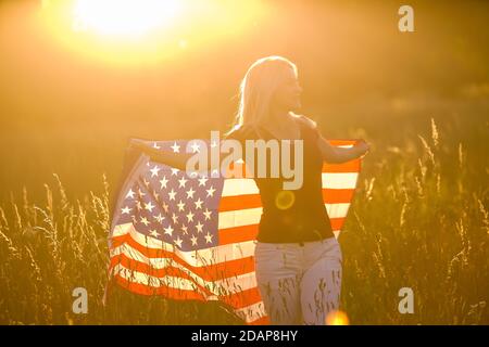 Jeune fille heureuse courir et sauter insouciante avec les bras ouverts sur le champ de blé. Drapeau des États-Unis. Image en tons. Mise au point sélective. Banque D'Images