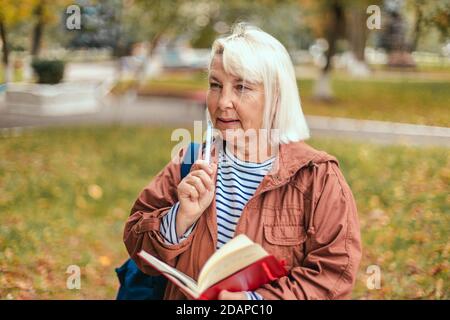 Portrait d'une femme âgée, concentrée et attentionnés, ayant un bloc-notes et un stylo entre les mains, planifiant, expert, analysant la marche dans le parc d'automne. Concept de publicité Banque D'Images