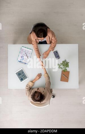 Vue de dessus de deux femmes d'affaires élégantes qui se branchiaient les mains sur le bureau après la négociation Banque D'Images