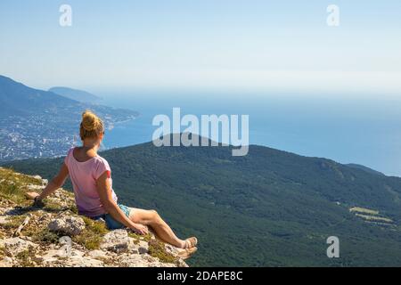Une femme blonde est assise au bord d'une montagne un matin d'été et regarde le lever du soleil Les montagnes et la mer en Crimée Banque D'Images
