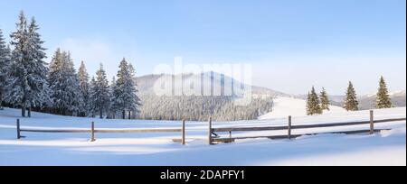 Paysage d'hiver. Clôture en bois. Vue panoramique. Magnifique paysage de hautes montagnes, forêt couverte de neige et ciel bleu. Fond d'écran arrière-plan enneigé Banque D'Images
