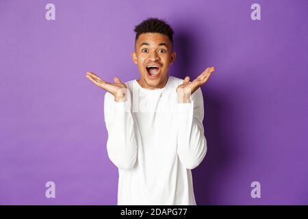 Image d'un beau jeune homme afro-américain, enthousiaste, réagissant à des nouvelles impressionnantes, impressionné par le fond violet Banque D'Images