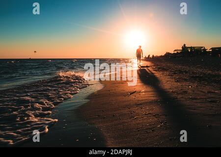 Une silhouette d'homme marchant sur le ciel lumineux du coucher du soleil au bord de la côte. Paysage d'été. Banque D'Images