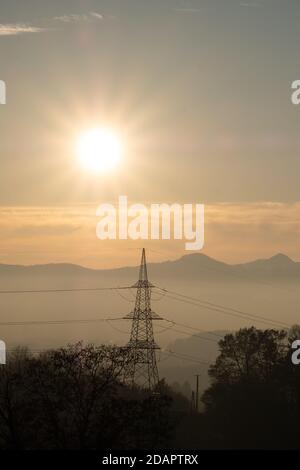 vue sur l'infrastructure électrique, la colonne de puissance et les câbles dans un paysage magnifique avec des montagnes brumeuses et le soleil couchant. Banque D'Images