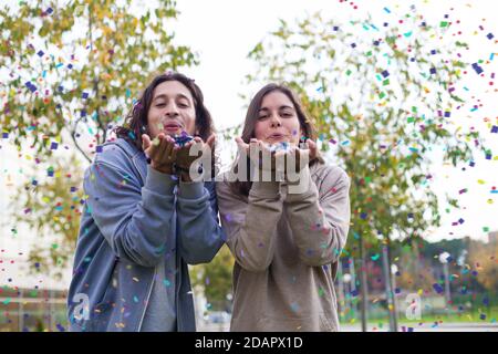deux jeunes amis soufflent des confettis des mains. Amis célébrant l'extérieur Banque D'Images