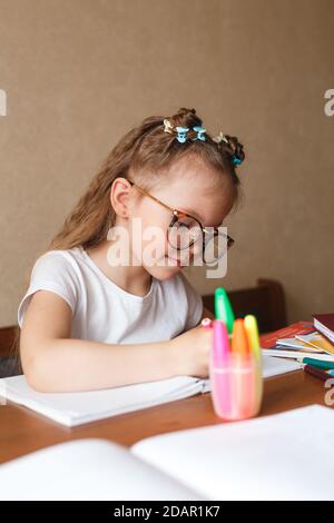 Petite fille intelligente assise à la table, écrivant des devoirs ou se préparant à l'examen. Banque D'Images