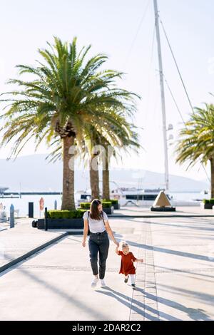 La mère et la fille sont main dans la main au milieu de la paume Arbres sur un quai à Porto Monténégro Banque D'Images