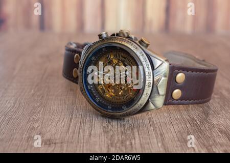 Montre-bracelet de style steampunk en bronze, acier, anneau intérieur bleu marine et maille de cuir marron sur une planche de bois. Vous pouvez voir la machine interne de t Banque D'Images