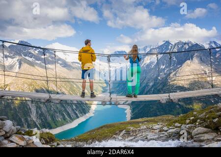 Randonneur, jeune femme et jeune homme sur le pont suspendu à Olpererhuette, réservoir Schlegeis, réservoir Schlegeis, Alpes de Zillertal, Schlegeiskees Banque D'Images