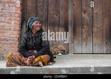 Femme âgée avec foulard et anneau de nez assis devant une porte en bois, Himalaya, Jiri, région de Khumbu, Népal Banque D'Images