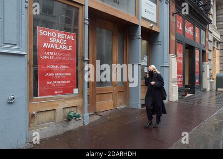 Manhattan, New York. 13 novembre 2020. Une femme portant un masque marche en face d'un magasin fermé à Soho avec un panneau lisant l'espace de vente disponible. Banque D'Images