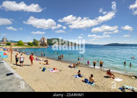 Les touristes et les habitants de la région se détendent sur la plage de sable de la ville le long du lac coeur d'Alene avec la station et Tubbs Hill en arrière-plan. Banque D'Images