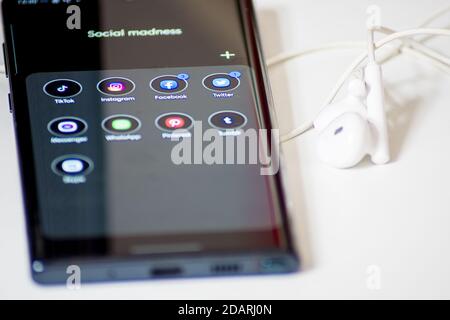 Vienne / Autriche / 13 novembre 2020 : smartphone noir brillant et écouteurs blancs sur le bureau blanc Banque D'Images