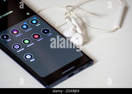 Vienne / Autriche / 13 novembre 2020 : smartphone noir avec applications de réseaux sociaux à côté des écouteurs blancs sur le bureau Banque D'Images