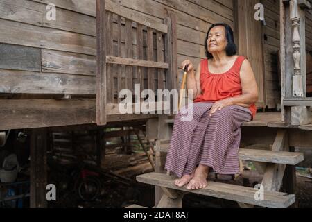 Femme thaïlandaise âgée dans un col rond sans manches assis seul ancienne maison en bois Banque D'Images