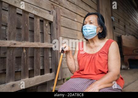 Femme thaïlandaise âgée en col rond sans manches portant un masque médical pour protéger la pandémie du virus corona (covid-19) dans une ancienne maison en bois Banque D'Images