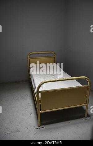 cellule d'isolement abandonnée dans un hôpital, sujet chaud en psychiatrie, punition, cellule solitaire, fond gris avec lit cloué au sol. Banque D'Images