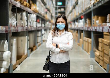 femme portant un masque médical avec les bras croisés dans l'entrepôt pendant la pandémie du coronavirus (covid-19). Banque D'Images