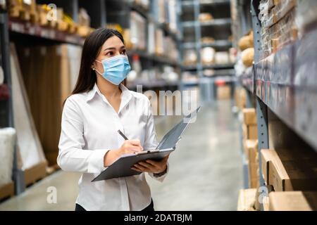 femme employée avec masque médical tenant le presse-papiers et vérifiant l'inventaire dans l'entrepôt pendant la pandémie du coronavirus (covid-19) Banque D'Images