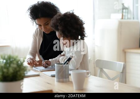 S'occuper de mère afro-américaine aider la petite fille à faire ses devoirs Banque D'Images