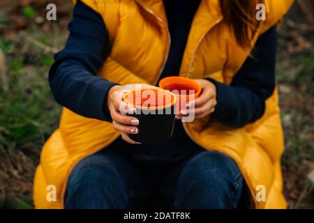 Boire du thé pendant la randonnée. Femme qui donne une tasse de thé chaud à partir d'une bouteille de thermos noire. Rafraîchissements pendant la randonnée Banque D'Images