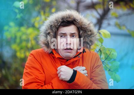 Portrait d'un homme adulte dans la capuche et veste orange s'accrochant au froid en automne. Un drôle de homme a gelé en se tenant dans la rue par temps froid Banque D'Images