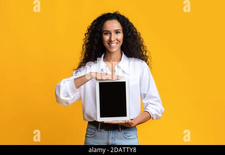 Belle femme souriante tenant une tablette numérique avec écran noir vierge Banque D'Images
