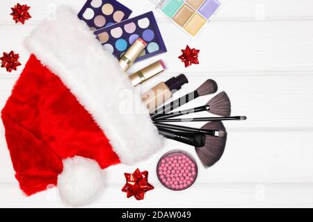 Produits de maquillage en chapeau de père Noël sur des planches en bois blanc - vue du dessus. Cosmétiques de maquillage comme concept de cadeau de Noël. Copier l'espace Banque D'Images